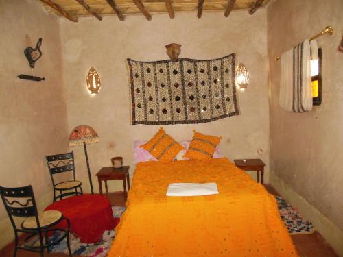 a bedroom with a large orange bed with two chairs at Kasbah Dar Dmana in Skoura