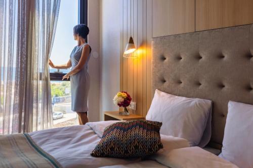 a woman standing in a bedroom looking out the window at Marina Burgas Hotel in Burgas City
