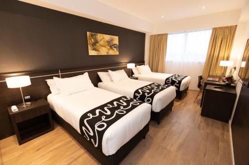 two beds in a hotel room with two lamps at Amerian Rafaela Hotel in Rafaela