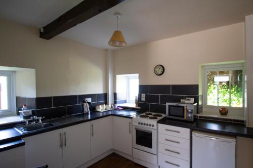 uma cozinha com armários brancos e um relógio na parede em Stone House Farm em St Bees