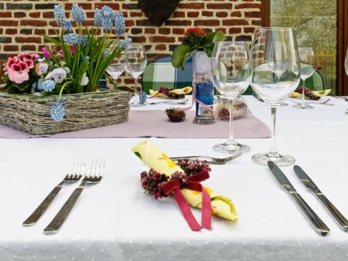 una mesa blanca con cubiertos, copas de vino y flores en B&B Aux Gaietés de la Sabotière, en Seloignes