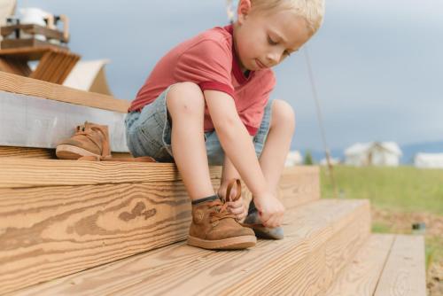 a little boy is putting on his shoes at Under Canvas West Yellowstone in West Yellowstone