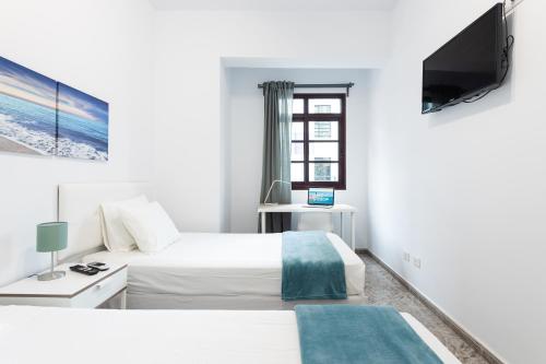 een witte slaapkamer met een bed en een televisie bij CoolivingC in Las Palmas de Gran Canaria