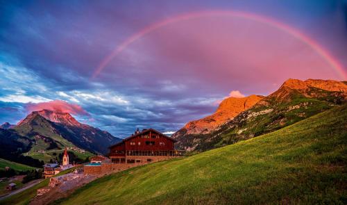 a rainbow over a mountain with a house on a hill at AlpenParks Hotel & Apartment Arlberg Warth mit Pool in Warth am Arlberg