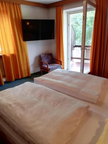 a bedroom with two beds and a tv and a chair at Hotel Rodes in Ortisei