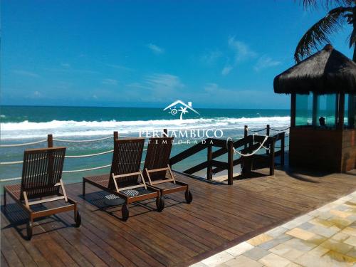 two chairs sitting on a wooden deck near the ocean at Beach Class Muro Alto - Porto de Galinhas in Porto De Galinhas