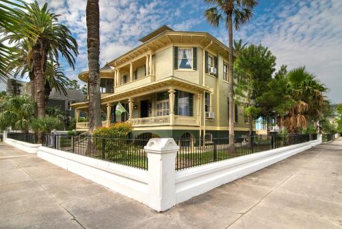 a yellow house with a black fence and palm trees at The Mansion on 17th, formerly Schaefer Haus in Galveston