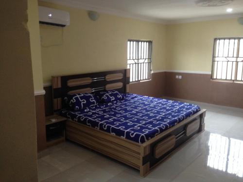 a bedroom with a bed with a blue comforter and windows at TJ Cottage in Ilorin