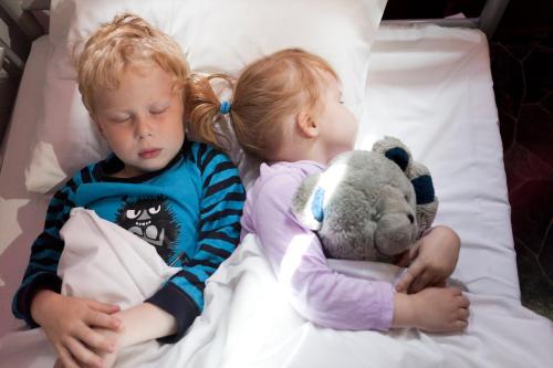two children laying in a bed with a teddy bear at Dream Hostel & Hotel Tampere in Tampere