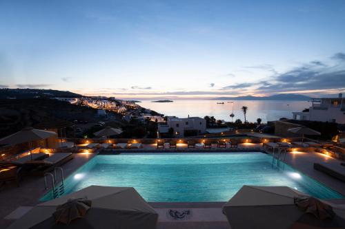 a swimming pool with a view of the ocean at night at Mykonos Bay Resort & Villas in Mýkonos City