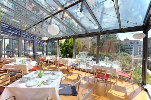 un restaurante con mesas y sillas blancas y ventanas en Abalon Hotel ideal en Stuttgart