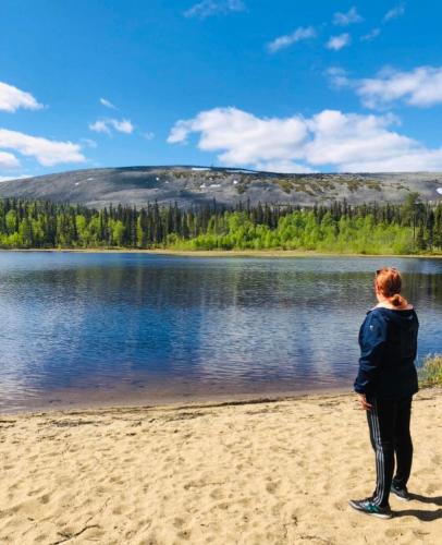 a woman standing on the beach looking at a lake at Villa Karhuntähti in Luosto
