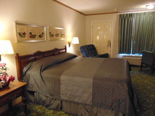 Heritage House Inn في Muleshoe: غرفه فندقيه بسرير وكرسي ونافذه