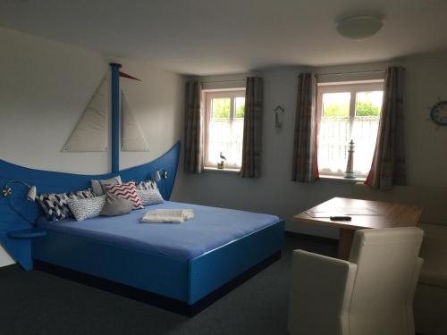 een slaapkamer met een blauw bed, een tafel en ramen bij Apartments im Sössaarep's Hüs in Nebel