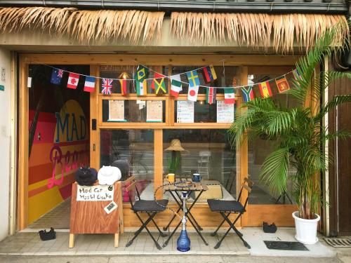 frente de una tienda con mesa, sillas y banderas en Mad Cat Hostel Osaka & Bar, en Osaka