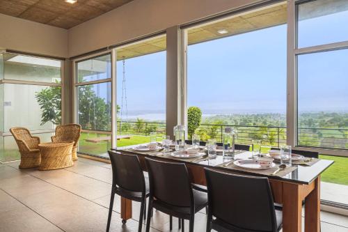 a dining room with a table and chairs and large windows at SaffronStays Serenity, Igatpuri in Igatpuri