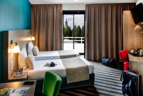 a hotel room with a bed and a desk and a window at Hôtel Panorama in Lourdes