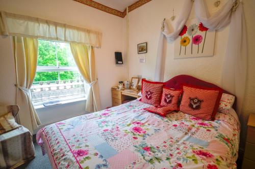 a bedroom with a bed with red pillows and a window at Gorphwysfa House B & B in Betws-y-coed