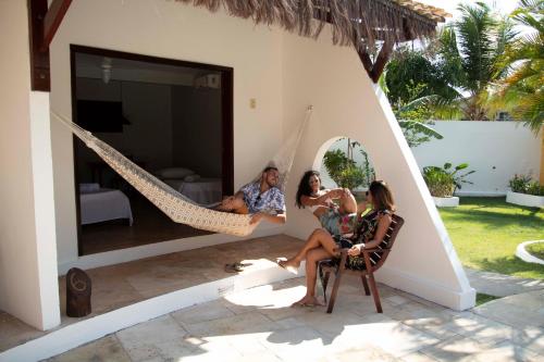 a man and two women sitting in a hammock on a house at Pousada Porto Azul in Cumbuco