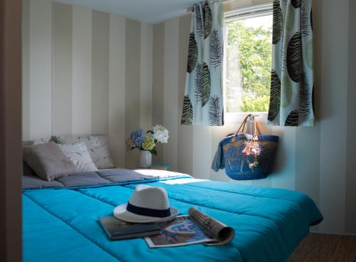 a bedroom with a blue bed with a hat and a window at Camping Officiel Siblu Les Sables du Midi in Valras-Plage