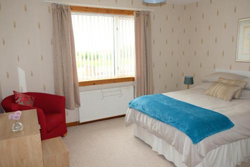 a bedroom with a bed and a red chair and a window at Druimard, Lower Barvas, Isle of Lewis in Barvas