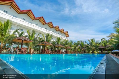 einem großen Pool mit Stühlen und Sonnenschirmen vor einem Gebäude in der Unterkunft JKAB Beach Resort in Trincomalee