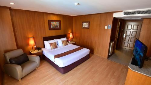a bedroom with a bed and a chair and a television at Dynasty Inn Pattaya in Pattaya Central