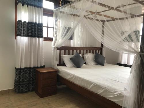 une chambre avec un lit à baldaquin avec des rideaux blancs dans l'établissement The Dalawella Porch House, à Galle