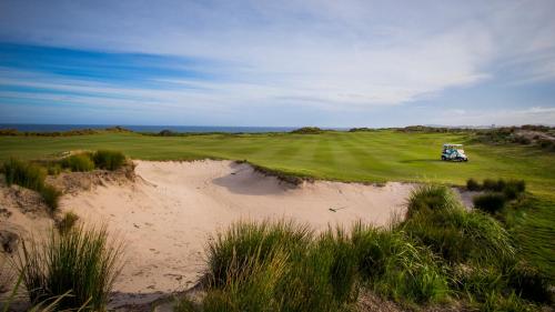 a golf course with a sand dune next to a green at Pullman Magenta Shores Resort in The Entrance