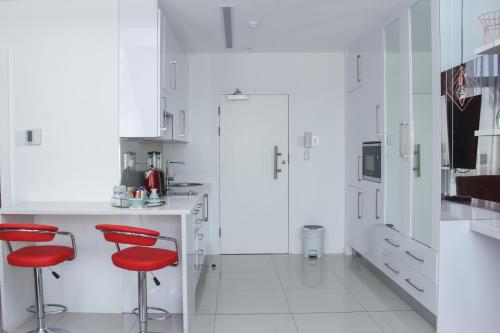 Biała kuchnia z czerwonymi stołkami i lodówką w obiekcie Green Avenue Apartments w mieście Gaborone