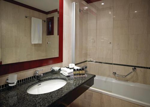 y baño con lavabo, espejo y bañera. en Roda Beach Resort & Spa, en Karousádes