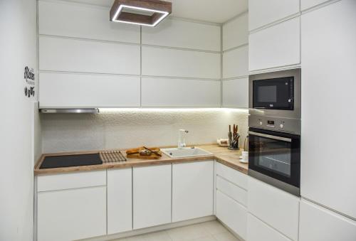 eine weiße Küche mit einer Spüle und einer Mikrowelle in der Unterkunft Lux Apartment Flatiron Skopje in Skopje