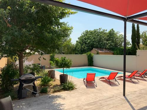 a swimming pool with red chairs and an umbrella at La Maison de Caillette in Camaret-sur-Aigues