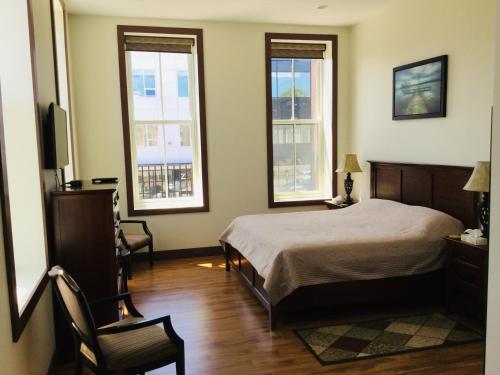 a bedroom with a bed and two windows and a chair at Water Suites in Charlottetown