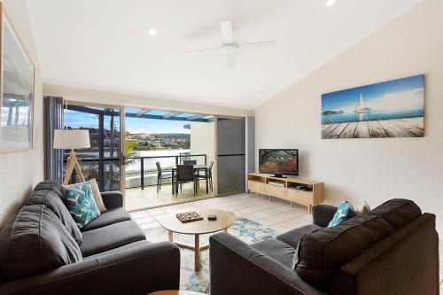 a living room with a couch and a tv and a table at Sails Luxury Apartments Merimbula in Merimbula