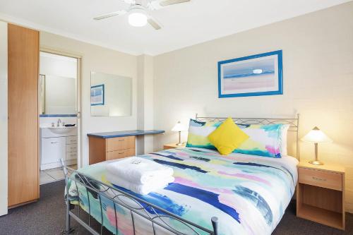 a bedroom with a colorful bed and a bathroom at Sails Luxury Apartments Merimbula in Merimbula