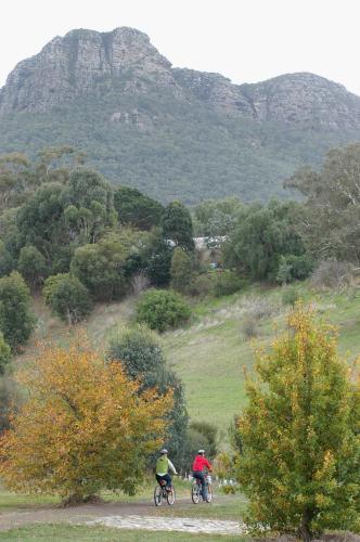 two people riding bikes down a dirt road with mountains in the background at Dunkeld Village Accommodation - formally Dunkeld Studio Accommodation in Dunkeld