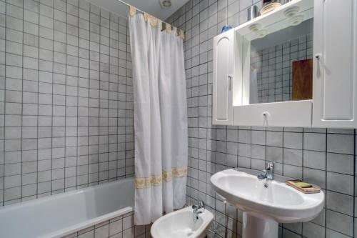 a white tiled bathroom with a sink and a mirror at Apartamento San Antonio in Benamahoma