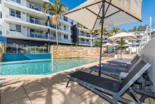 a pool with two lounge chairs and an umbrella at Mantra Nelson Bay in Nelson Bay