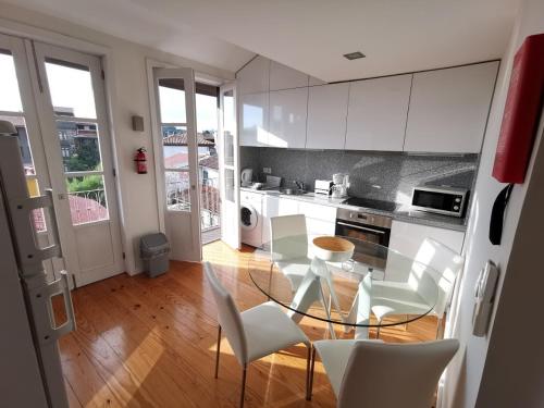 uma cozinha com uma mesa de vidro e cadeiras brancas em Mezzanine Apartment em Guimarães