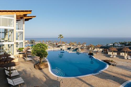 a large swimming pool next to a building and the ocean at Alua Village Fuerteventura - All Inclusive in Playa Jandia