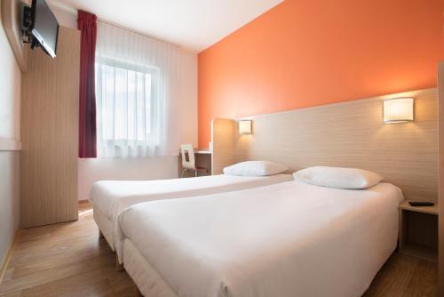 two beds in a hotel room with orange walls at Premiere Classe Wroclaw Centrum in Wrocław