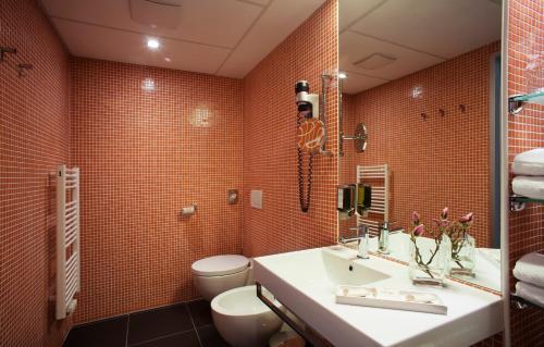 a bathroom with a sink and a toilet and orange tiles at Hotel Thermana Park Laško**** Superior in Laško