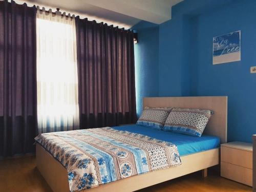 um quarto com uma cama com paredes azuis e uma janela em Lovely Apt at the heart of the city&near the lake em Pogradec