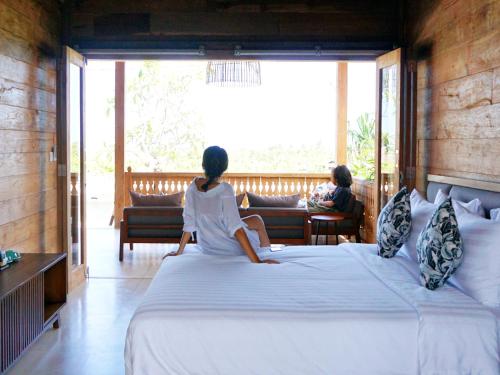 Dos mujeres sentadas en una cama mirando por la ventana en Rimbun Canggu Villa, en Canggu