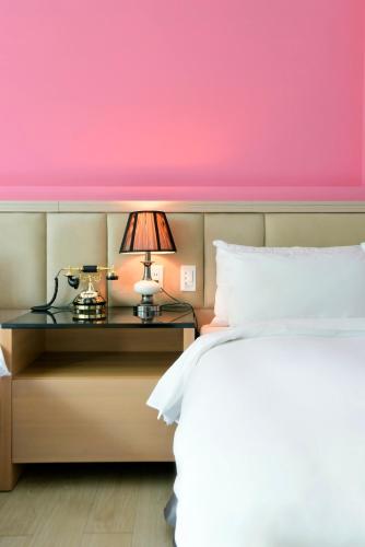 a bedroom with a pink wall and a bed with a lamp at Hotel Champs Elysées in Taichung