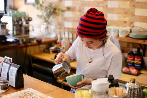 a woman in a kitchen pouring food into a bowl at Greenwood Hostel in Izumi-Sano