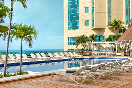 - une piscine avec des chaises longues et l'océan dans l'établissement Catalonia Santo Domingo, à Saint-Domingue
