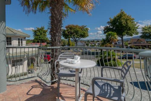 a table and chairs on a balcony with a palm tree at Silver Fern Rotorua Suites & Spa in Rotorua