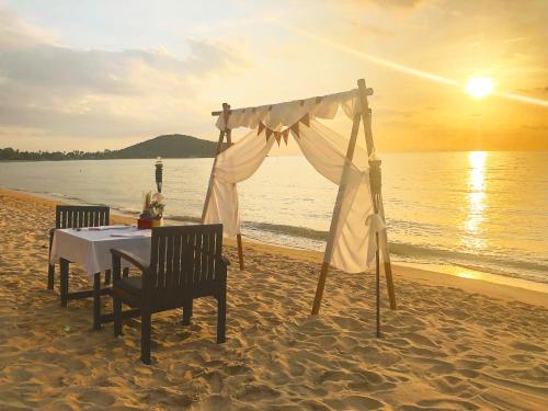 einen Tisch und Stühle am Strand mit Sonnenuntergang in der Unterkunft Kanok Buri Resort in Lipa Noi